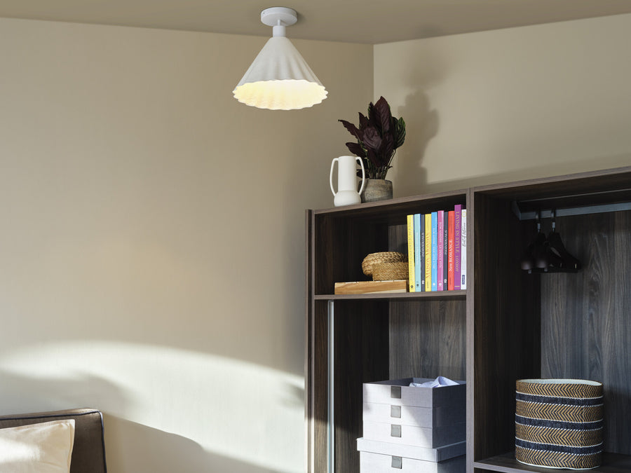 Plafonnier blanc allumé dans une pièce avec étagère, livres et plante.