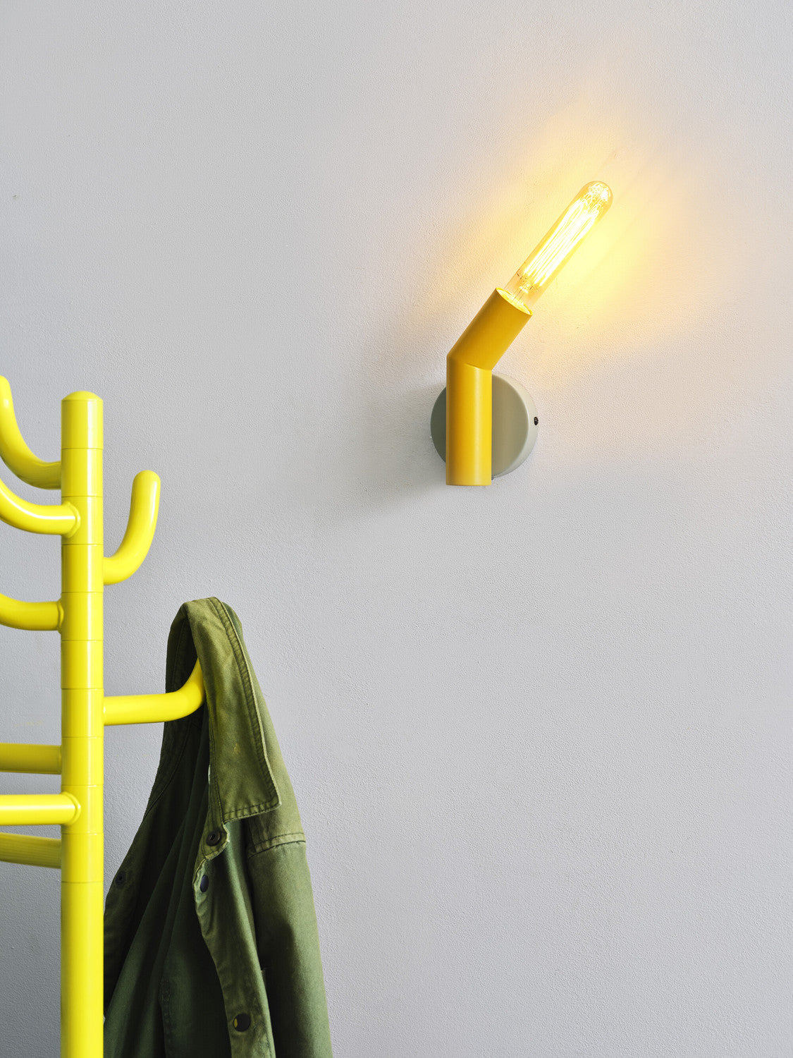 Gros plan de l’applique allumée sur mur blanc, ampoule filament et portemanteau flou.