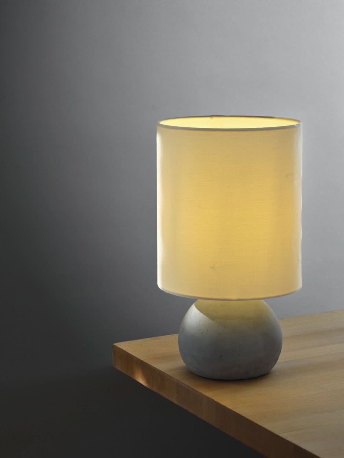 Gros plan de la lampe allumée, abat-jour beige lumineux posé sur un meuble en bois.