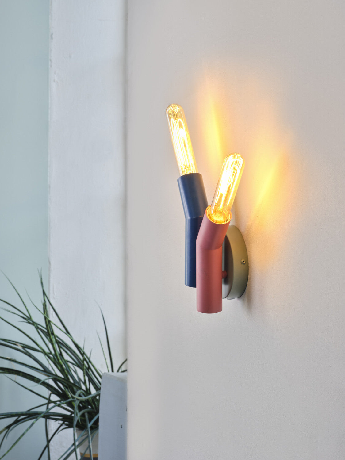 Gros plan de l'applique allumée avec deux ampoules visibles et ombre chaude.