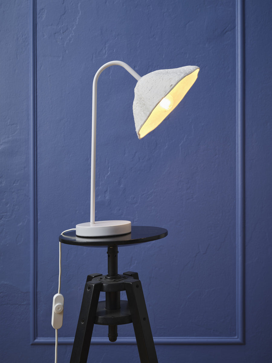 Vue rapprochée de la lampe allumée posée sur un guéridon noir, fond bleu.