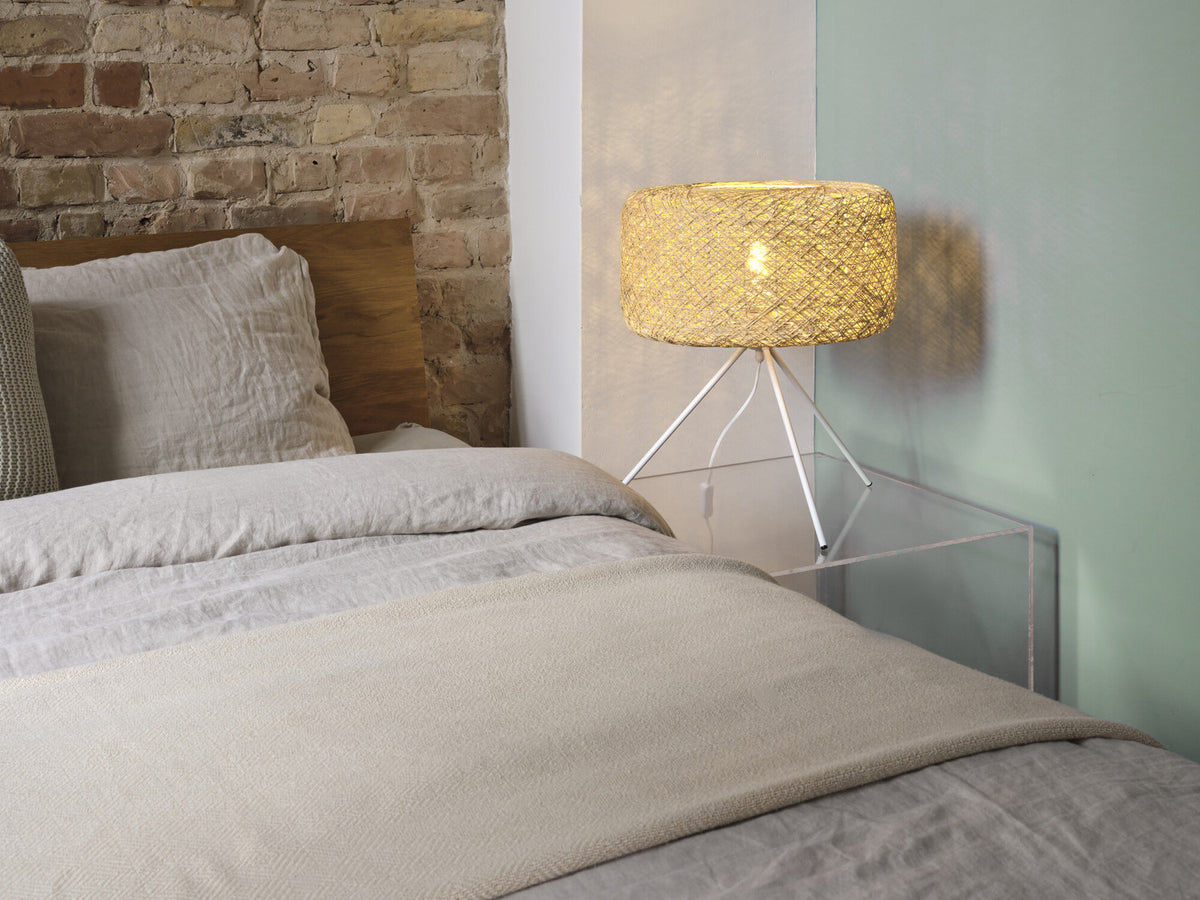 Lampe à poser allumée sur une table de chevet près d'un lit et mur en briques.