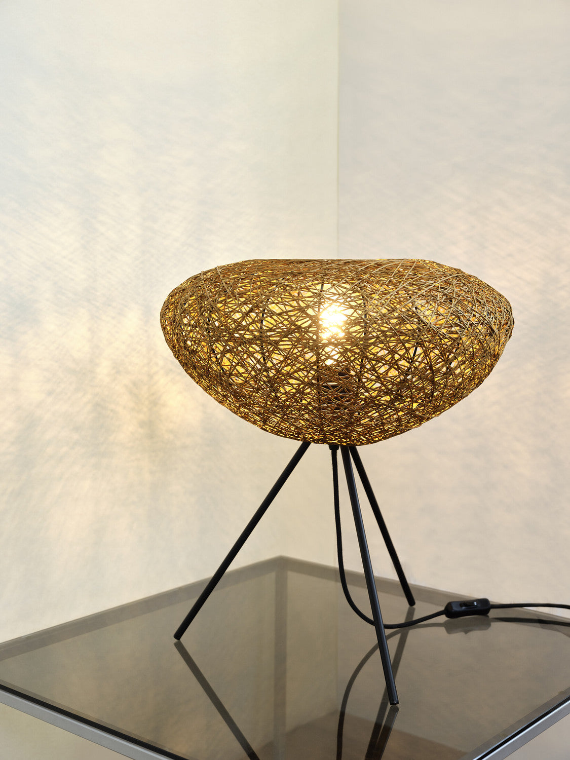 Gros plan de la lampe allumée posée sur une table en verre, lumière chaude.