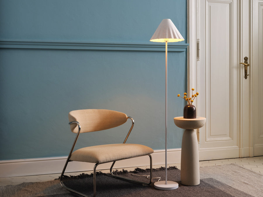 Lampadaire blanc allumé dans un salon, près d'une chaise et d'une table d'appoint.