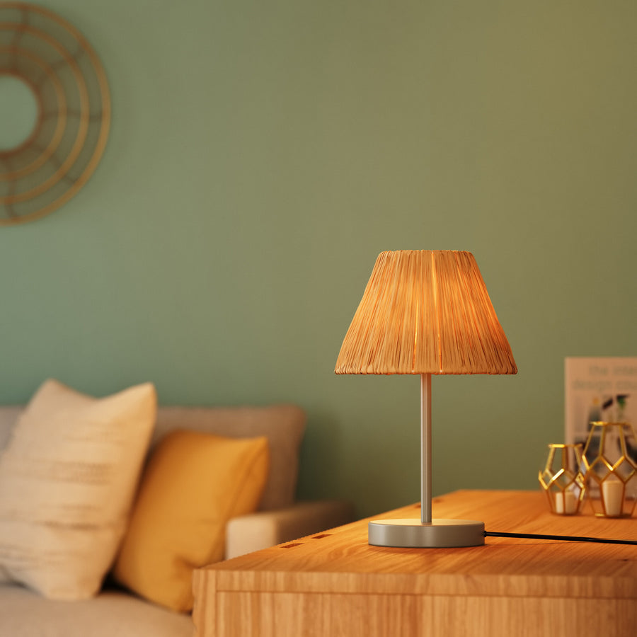 Gros plan de la lampe allumée sur une table en bois, mur vert et canapé flous.