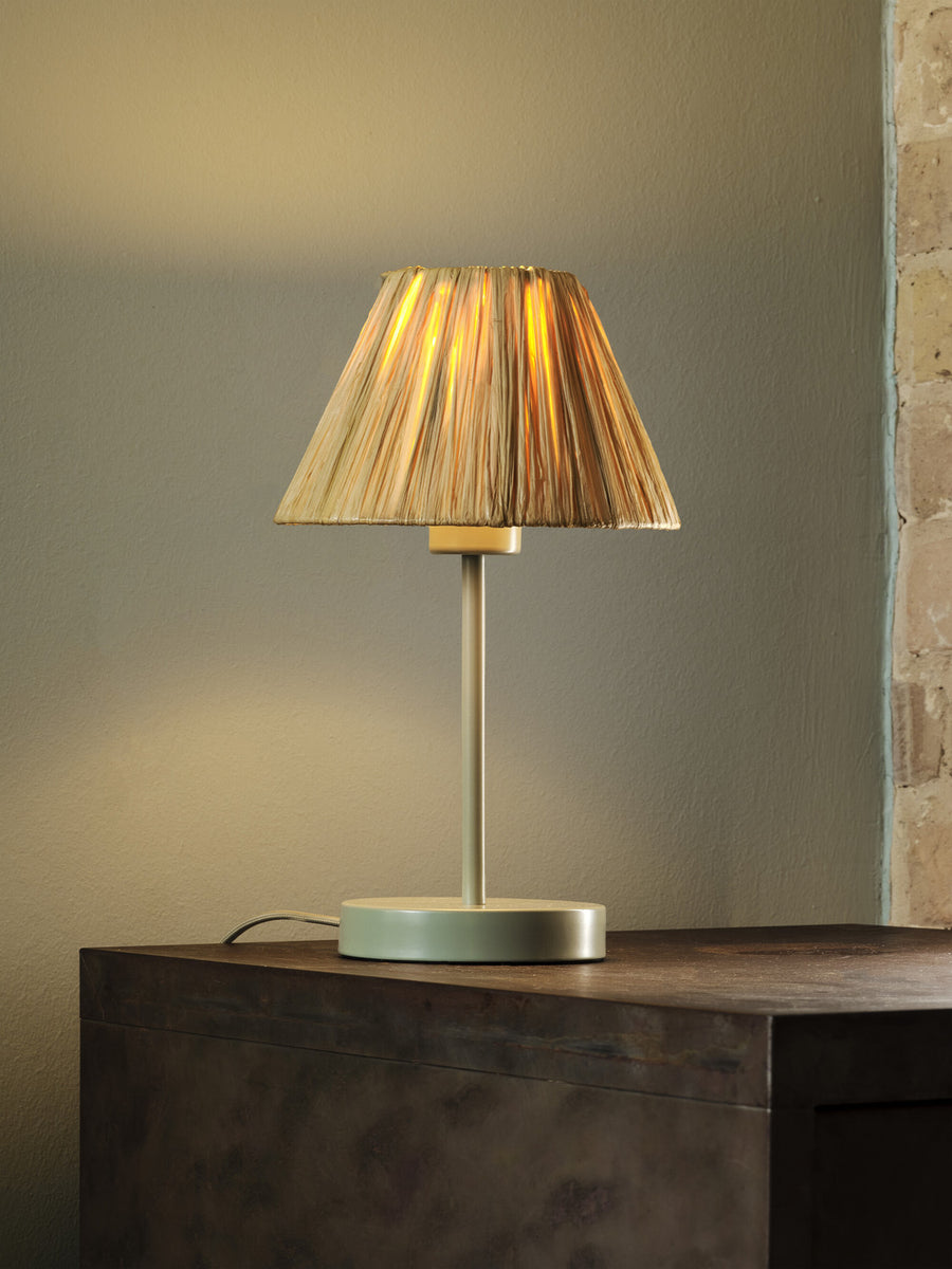 Lampe allumée sur un meuble en bois sombre, mur neutre et câble d'alimentation visible.