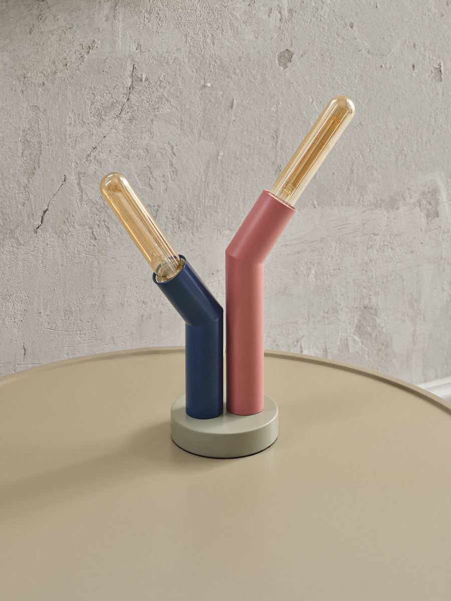Détail des deux bras tubulaires allumés, bleu et rose, sur base grise posée.