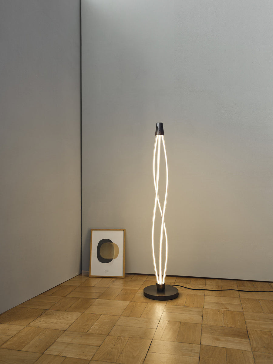 Lampadaire allumé dans un coin, près d'une affiche encadrée sur parquet.