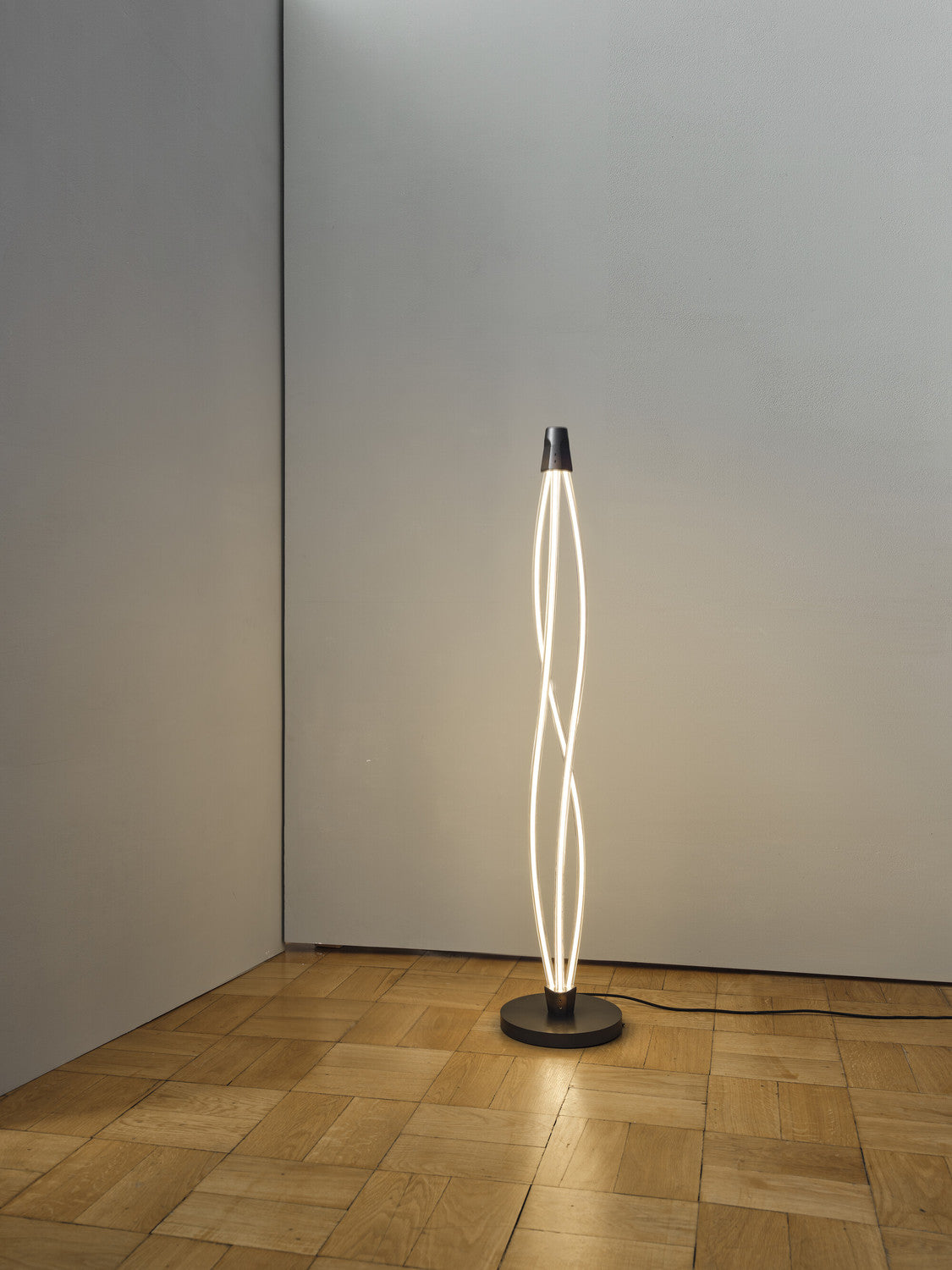 Lampadaire lumineux seul dans un angle de pièce, mur gris et parquet.