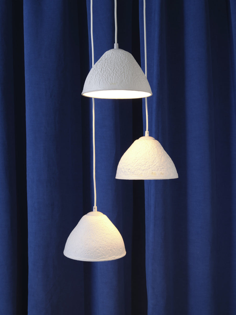 Détail des trois abat-jour suspendus à des hauteurs variées devant un tissu bleu.