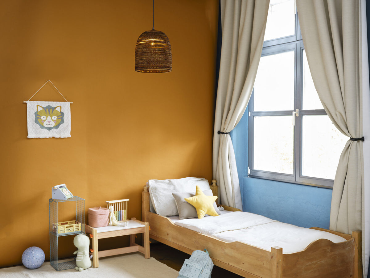 Mise en ambiance dans une chambre d'enfant au mur ocre, suspension allumée.