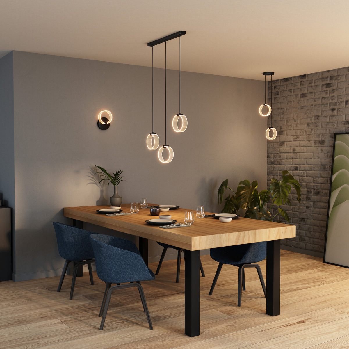 Ambiance repas avec suspension circulaire noire éclairant chaleureusement une table dressée en bois.