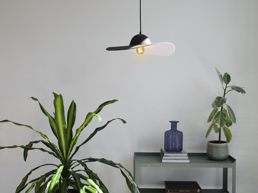 Suspension en feutre allumée au-dessus d'une console verte avec végétaux et vase.
