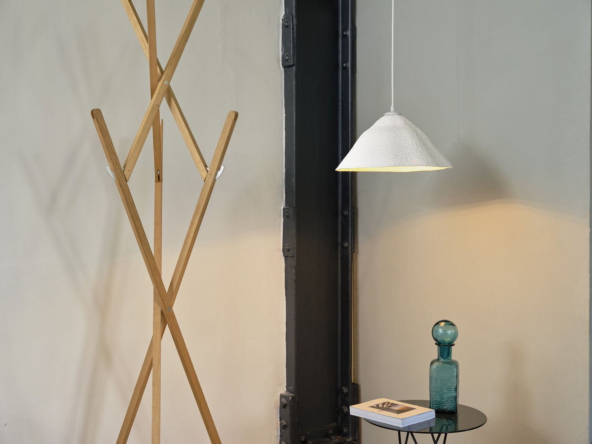 Mise en ambiance : suspension allumée près d'un portemanteau en bois et d'une petite table.