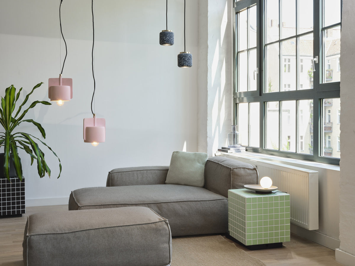 Mise en ambiance salon moderne, deux suspensions roses éclairées près d'une fenêtre et fauteuil gris.