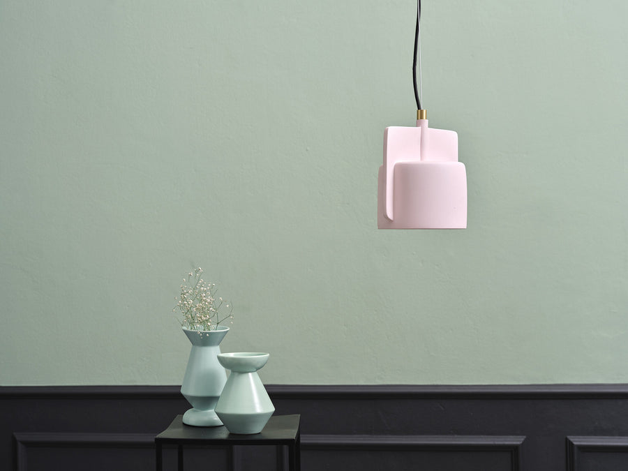 Suspension rose devant un mur vert sauge, deux vases céramiques sur une console noire.