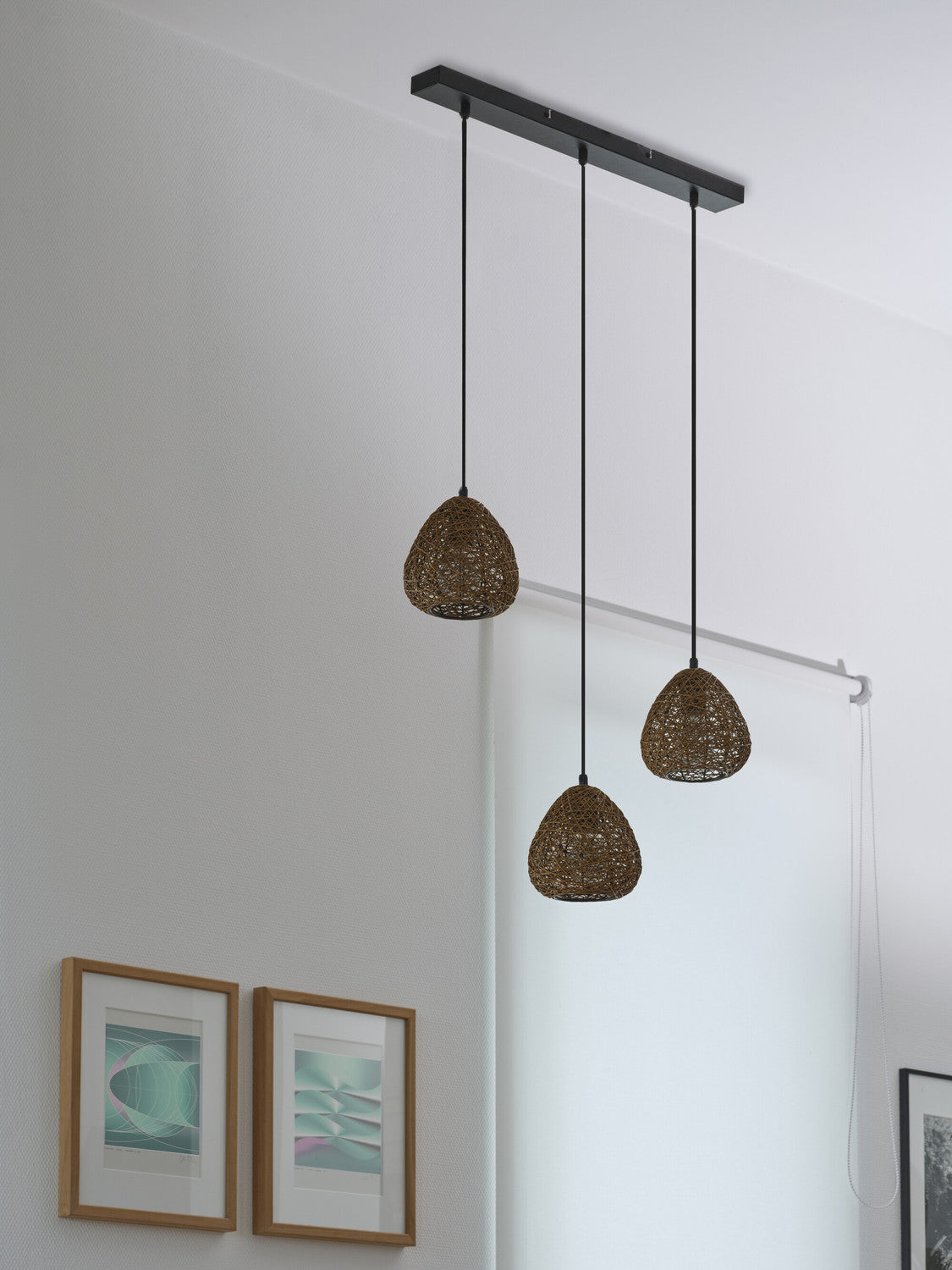 Suspension linéaire au plafond avec barre noire et trois cordons, devant un mur blanc et cadres.
