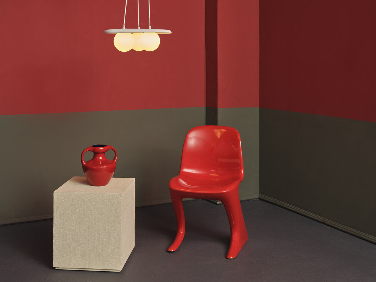 Suspension allumée dans une pièce colorée, près d'une chaise rouge.