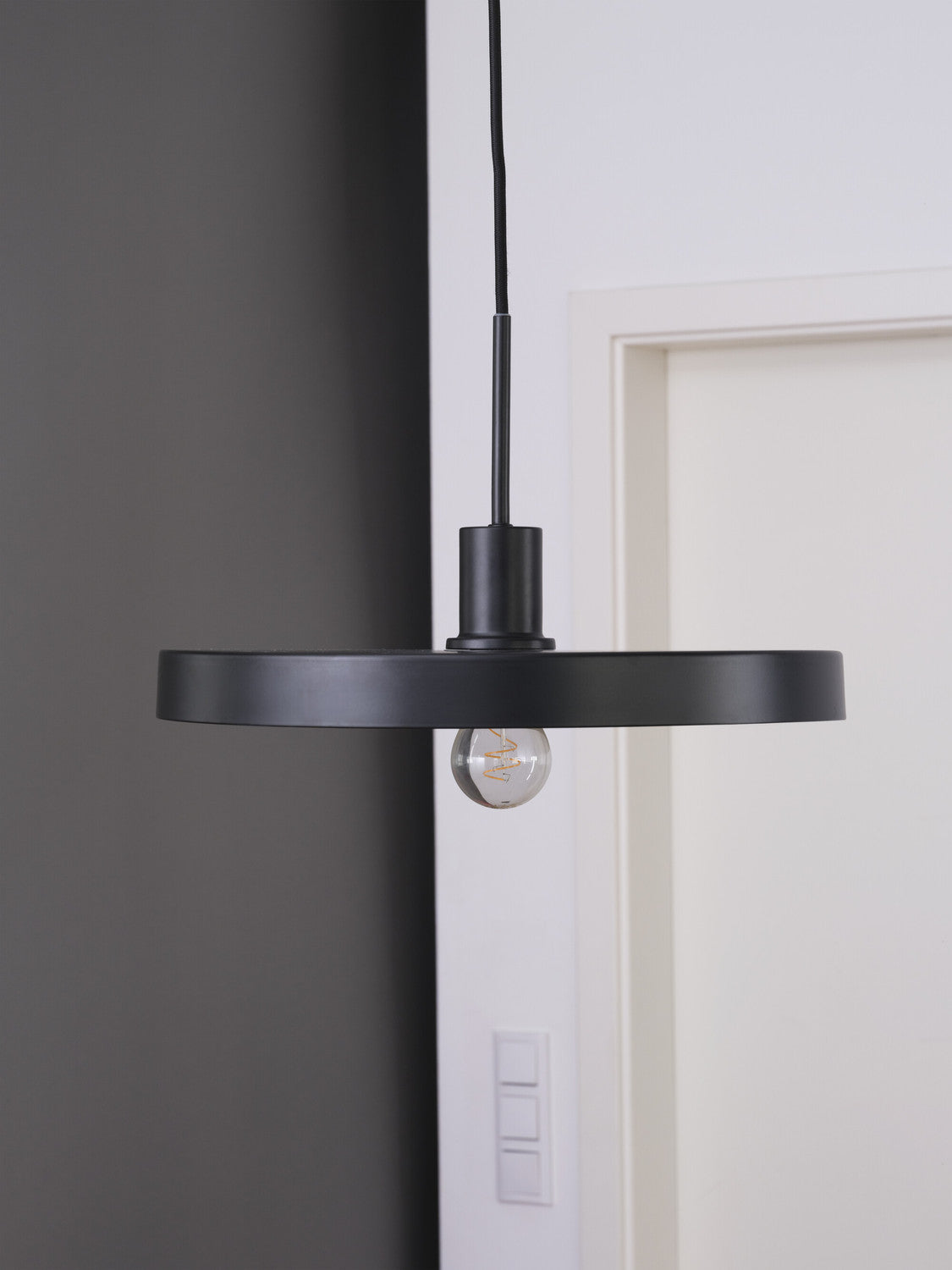 Vue de profil de la suspension noire avec son câble et ampoule.