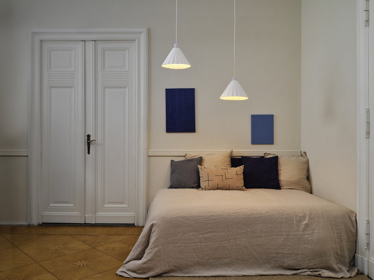 Deux suspensions blanches éclairent une chambre avec lit et portes.
