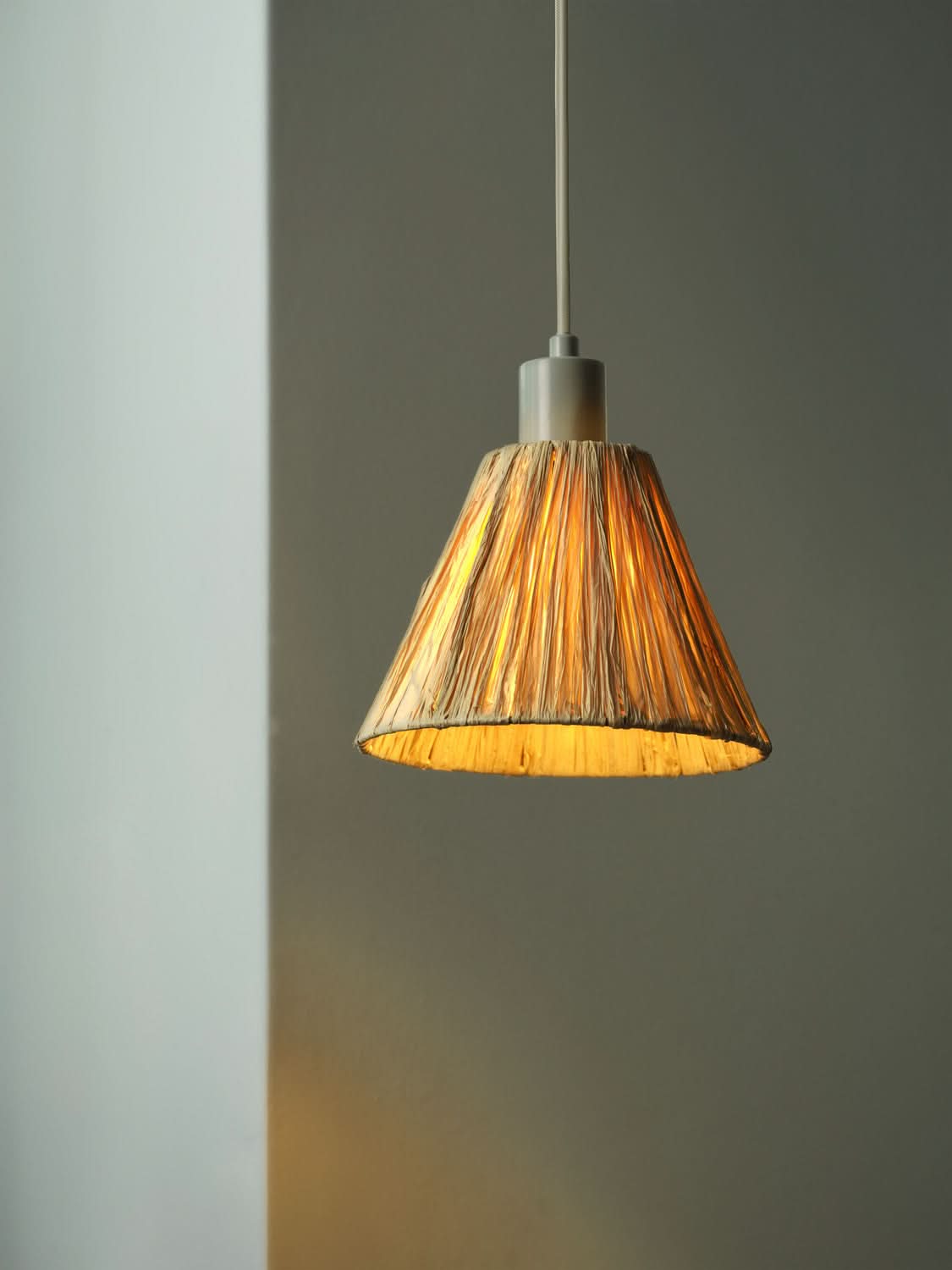 Détail de l'abat-jour conique en raphia diffusant une lumière chaude sur fond neutre.