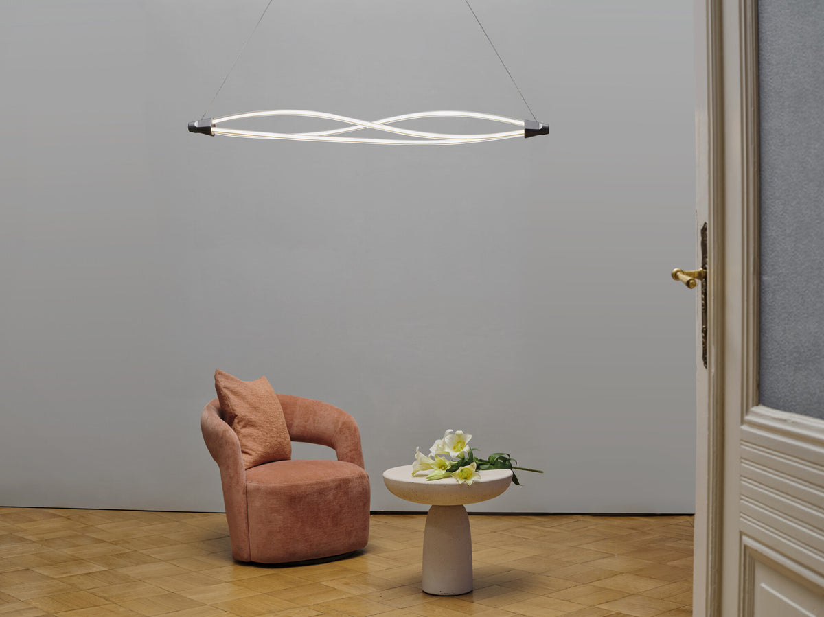 Mise en ambiance salon avec suspension allumée, fauteuil rose et table basse fleurie.