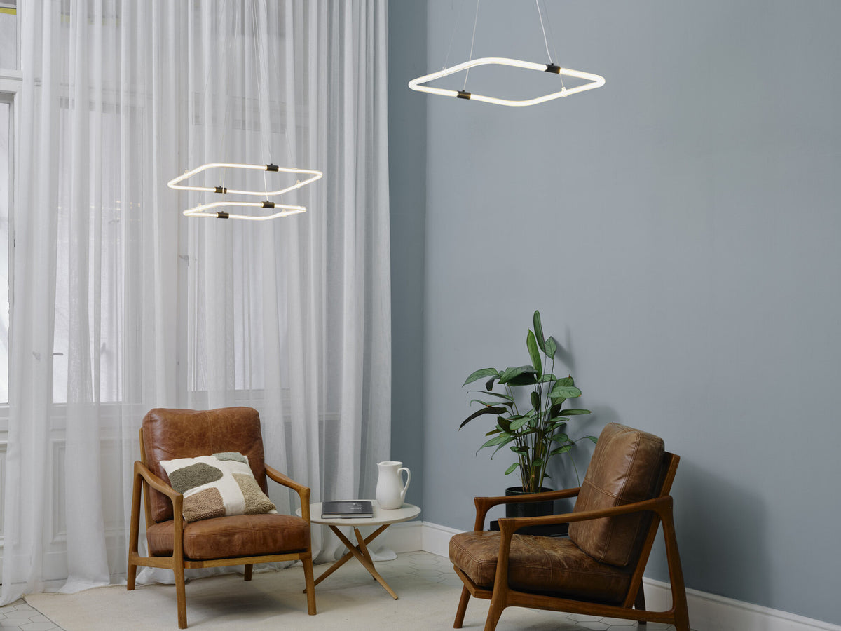 Plusieurs suspensions allumées dans un salon gris, au-dessus de fauteuils en cuir.