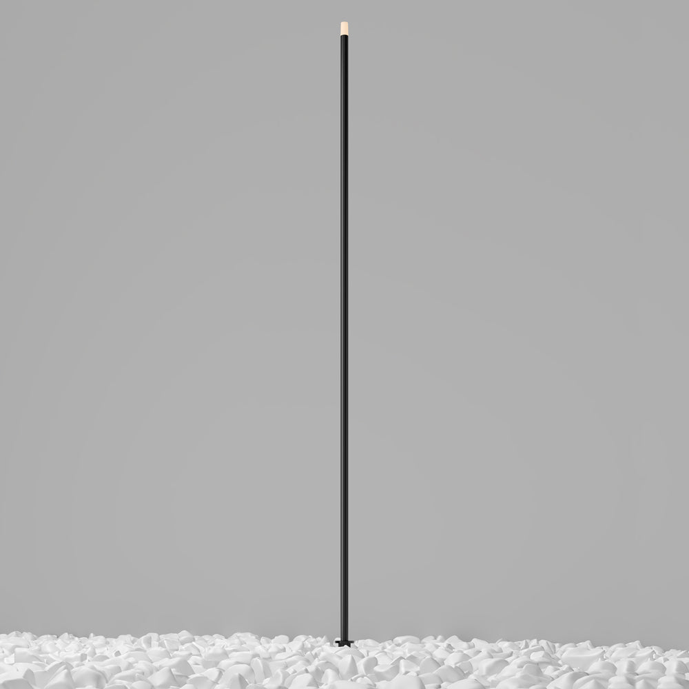 Luminaire à piquet noir de très grande hauteur, présenté de face sur galets blancs