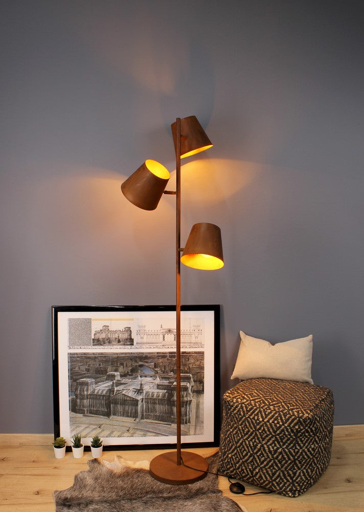 Lampadaire rouille en situation, près d'un pouf à motif géométrique et cadre noir.