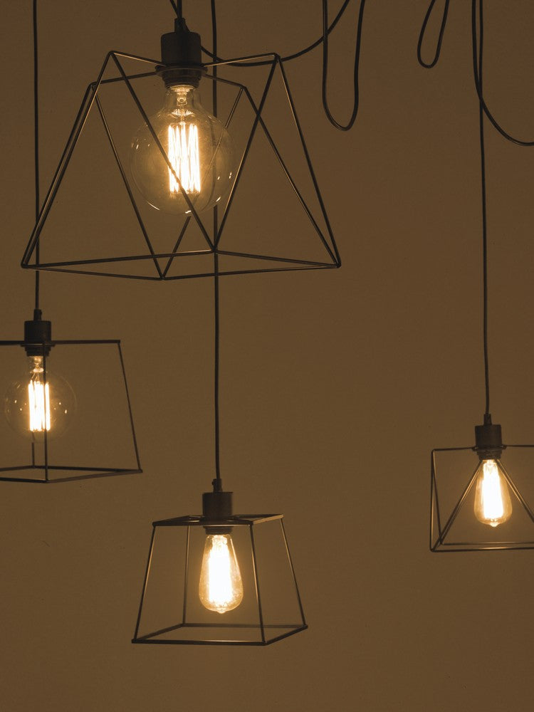 Mise en ambiance sombre avec plusieurs suspensions allumées, cages géométriques noires et ampoules filament