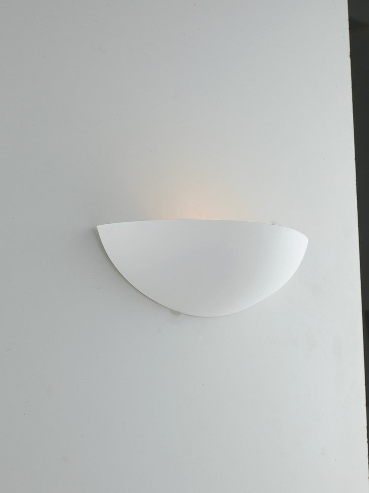 Applique fixée sur un mur blanc, allumée, diffusant une lumière chaude vers le haut