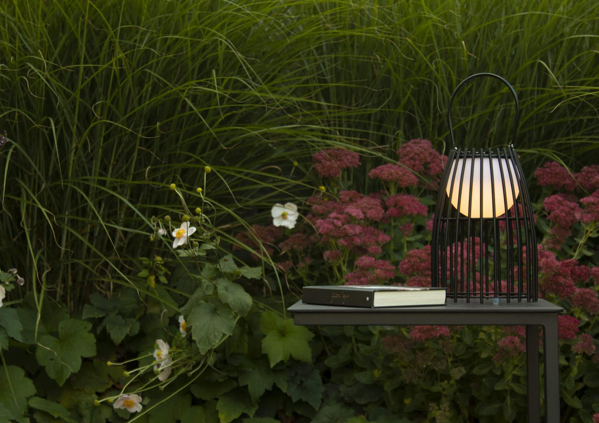 Vue rapprochée de la lampe noire allumée sur une table, entourée de fleurs roses.