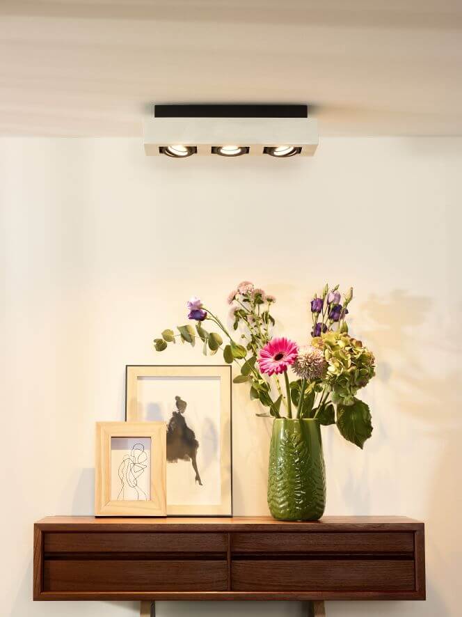 Vue rapprochée du luminaire blanc et noir éclairant un mur beige avec vase fleuri