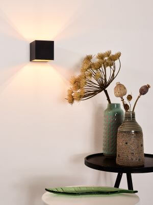 Applique murale noire allumée sur mur blanc, décorée de vases et fleurs séchées.