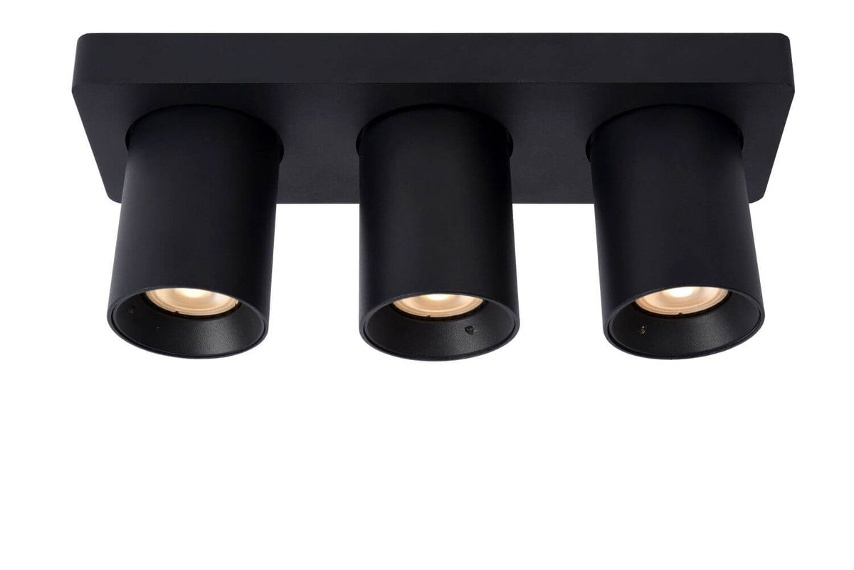 Vue de face du plafonnier, trois spots cylindriques noirs allumés, lumière chaude