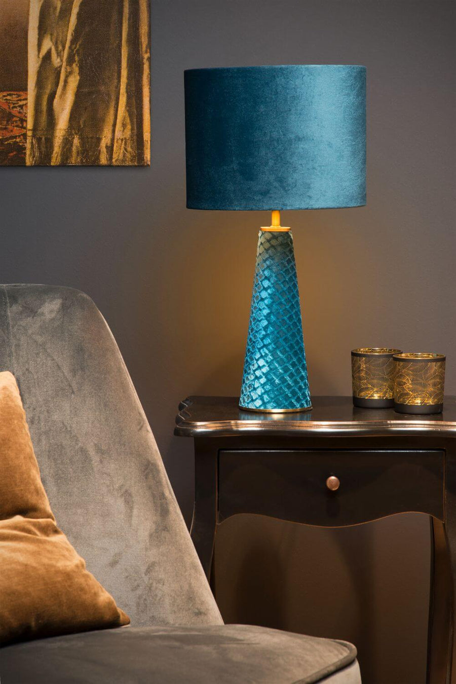 Lampe allumée sur une commode sombre, détail du tiroir et du coussin