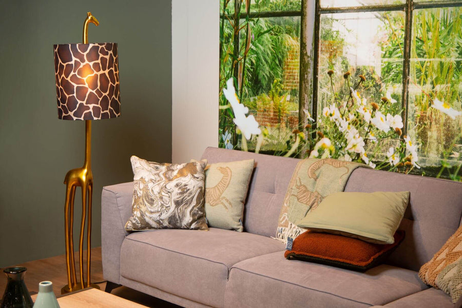 Vue rapprochée du lampadaire girafe doré et du canapé, coussins décoratifs.