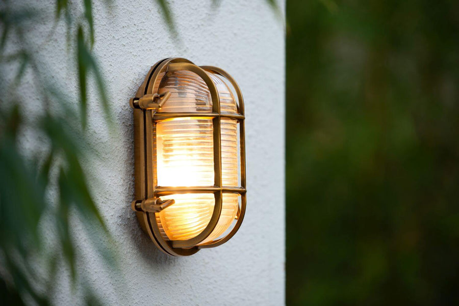 Gros plan sur l'applique dorée allumée, verre strié et grille métallique visibles.