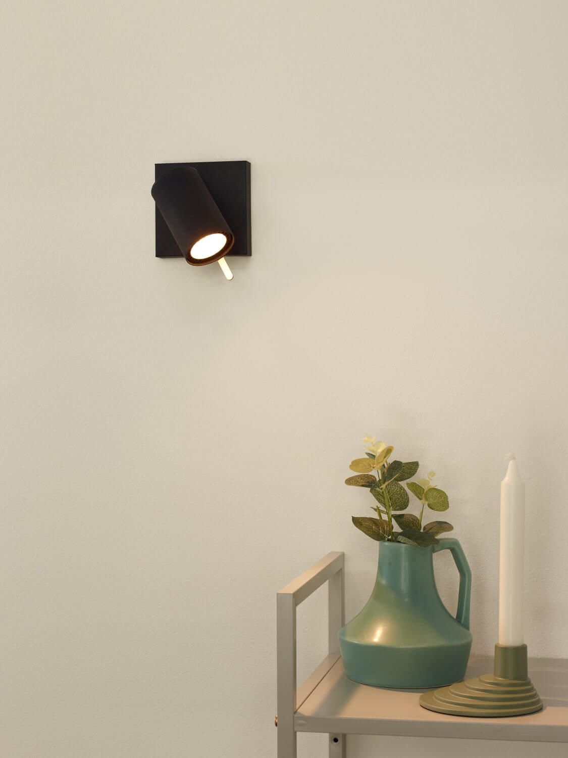 Spot cylindrique noir orientable monté sur mur blanc, ambiance chaleureuse