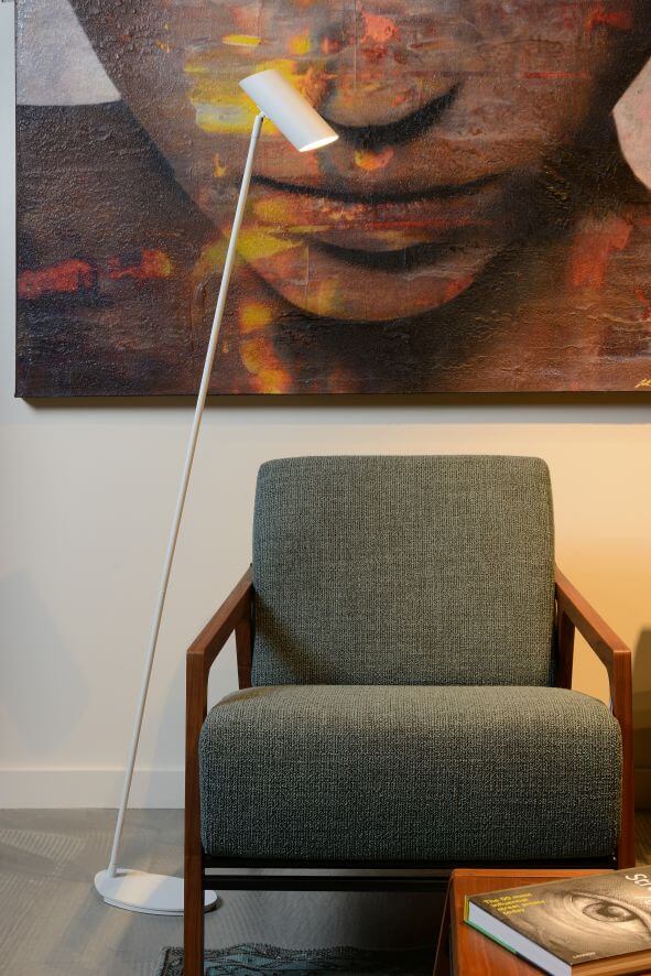 Lampadaire blanc élancé posé près d'un fauteuil vert et d'un tableau