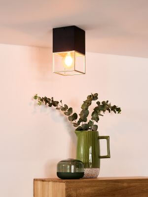 Plafonnier carré noir et doré installé au plafond dans une pièce claire avec vase et eucalyptus
