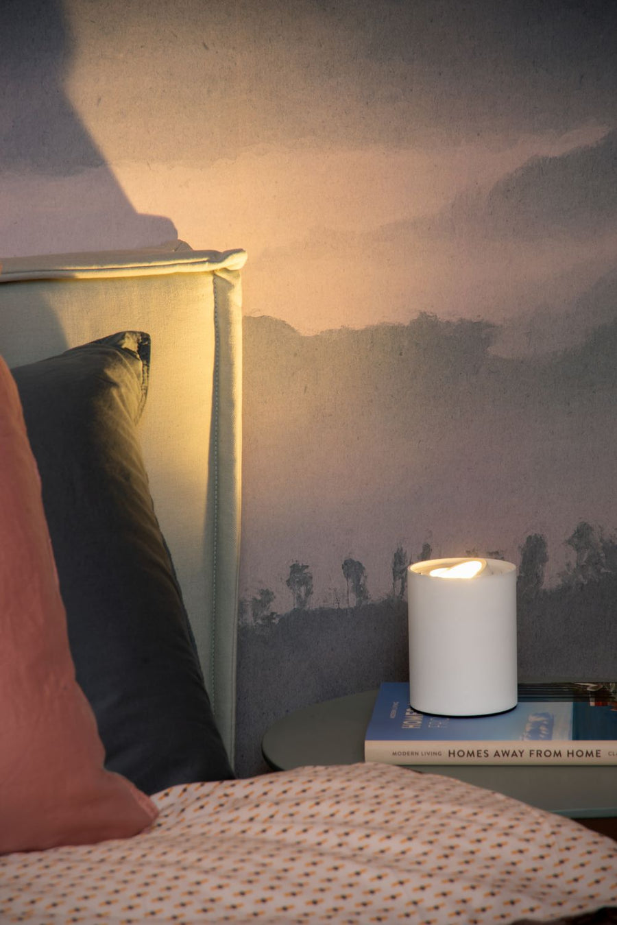 Gros plan de la lampe allumée près du lit, halo chaud sur le mur