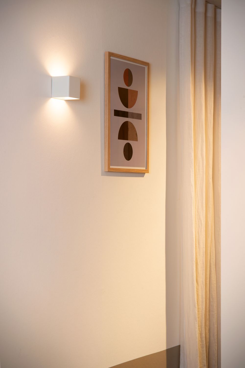Vue rapprochée de l'applique cube blanche sur mur, éclairant haut et bas.