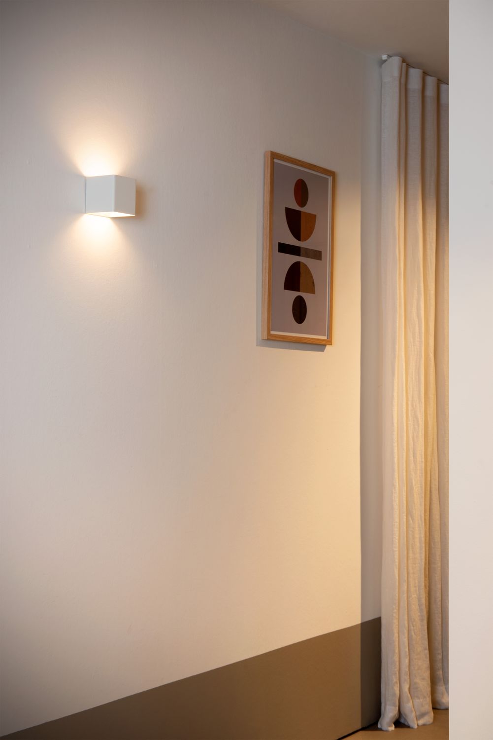 Mise en ambiance de l'applique murale blanche allumée, cadre décoratif et rideau.