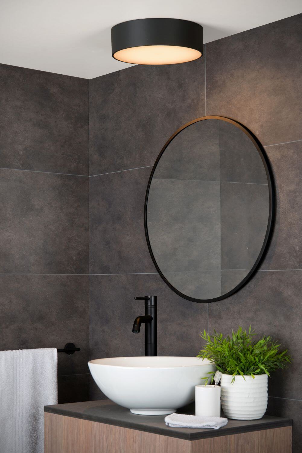 Vue rapprochée du plafonnier cylindrique noir installé au plafond dans une salle de bain.
