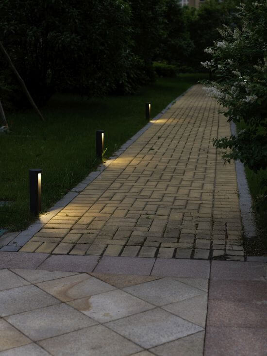 Chemin de jardin éclairé la nuit par plusieurs bornes noires alignées le long d'une allée pavée.