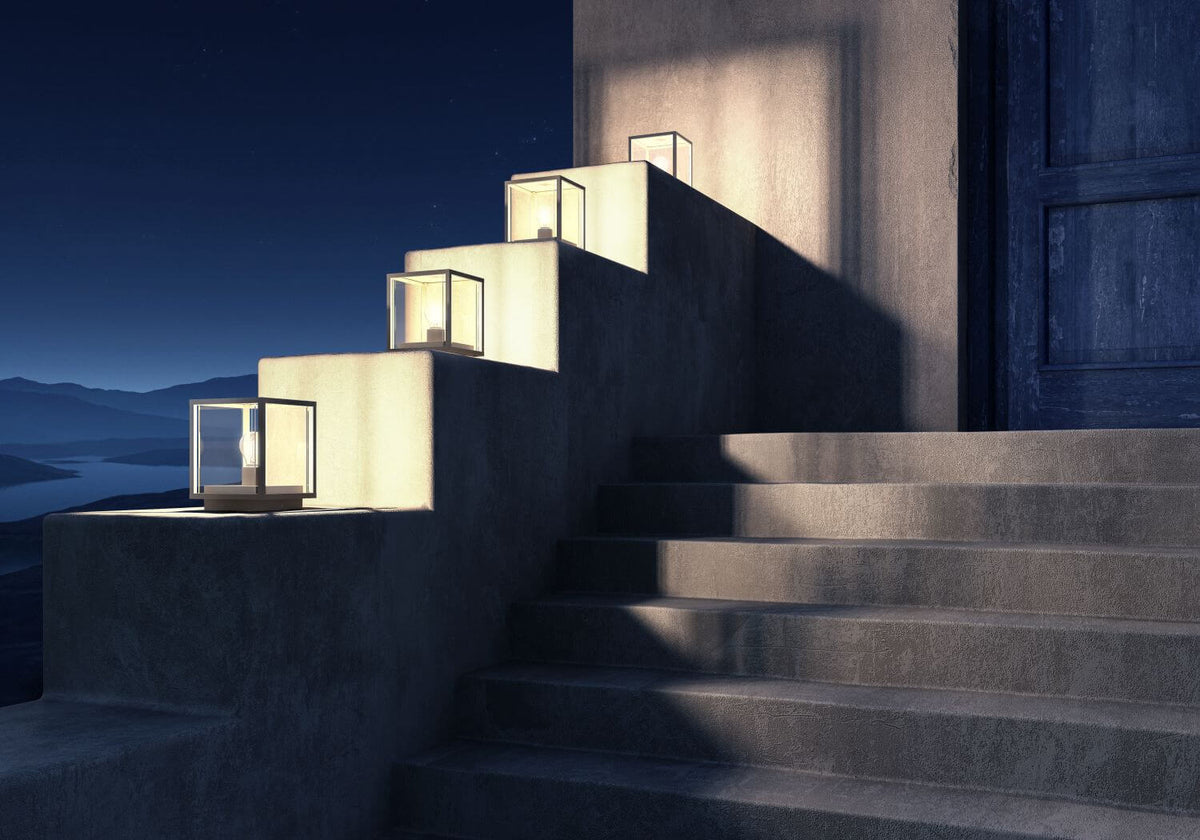Mise en ambiance nocturne de plusieurs bornes cubiques allumées alignées sur des marches en béton.