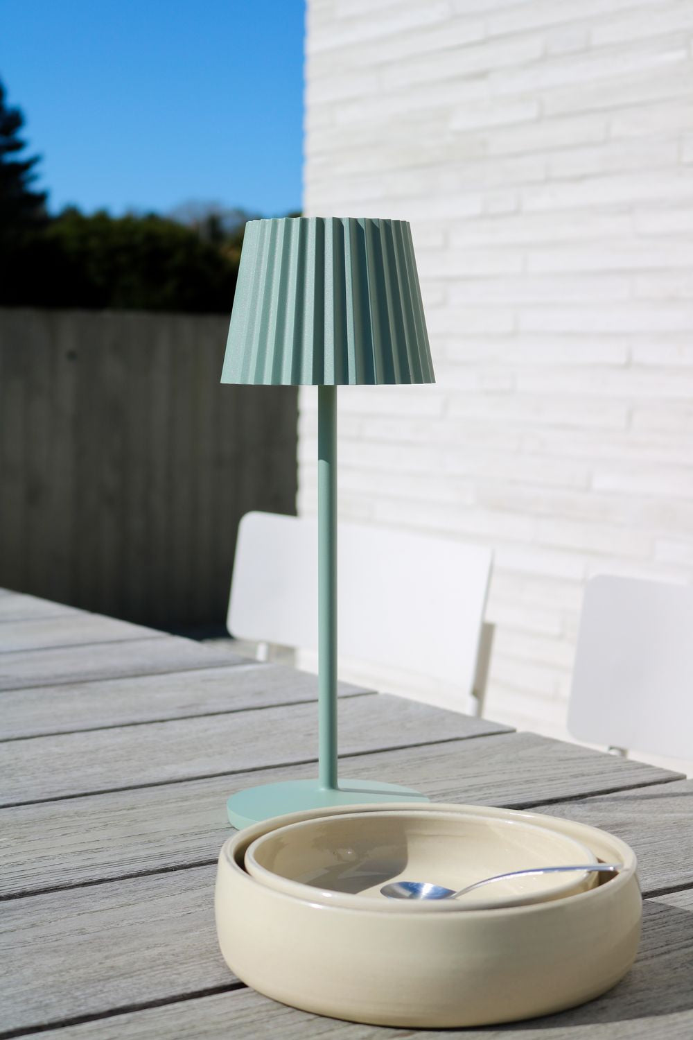 Mise en ambiance extérieure, lampe verte devant mur de briques blanches et ciel bleu