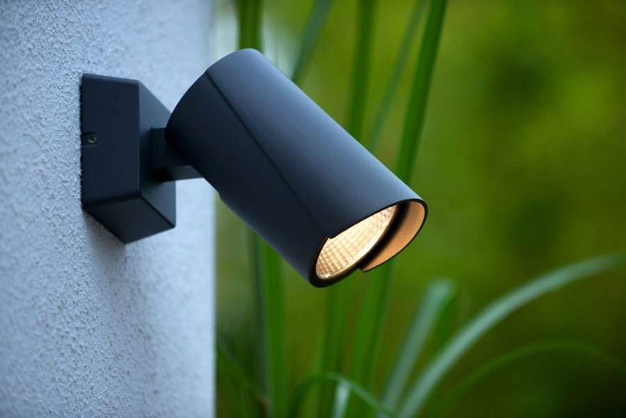Gros plan de l'applique cylindrique noire fixée au mur, feuillage vert flou