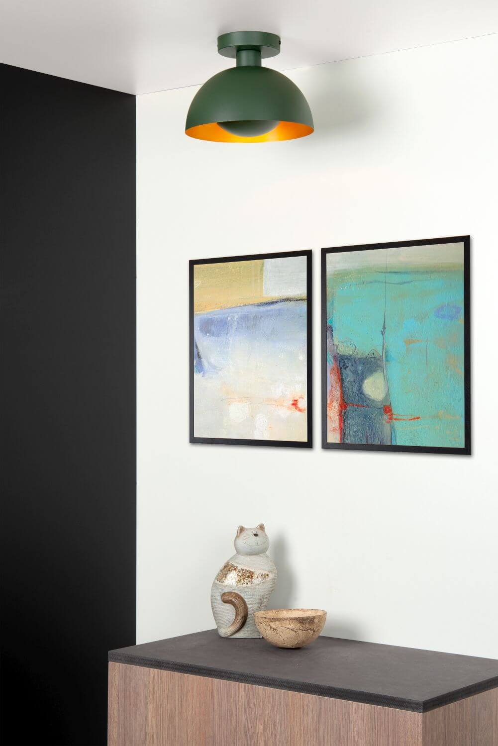 Plafonnier vert suspendu au plafond blanc au-dessus d’un meuble, tableaux abstraits au mur.